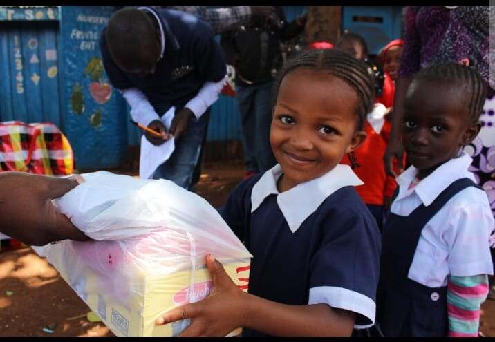 A schoolgirl smiling while receiving a box of sanitary pads at a dignity-kit distribution
