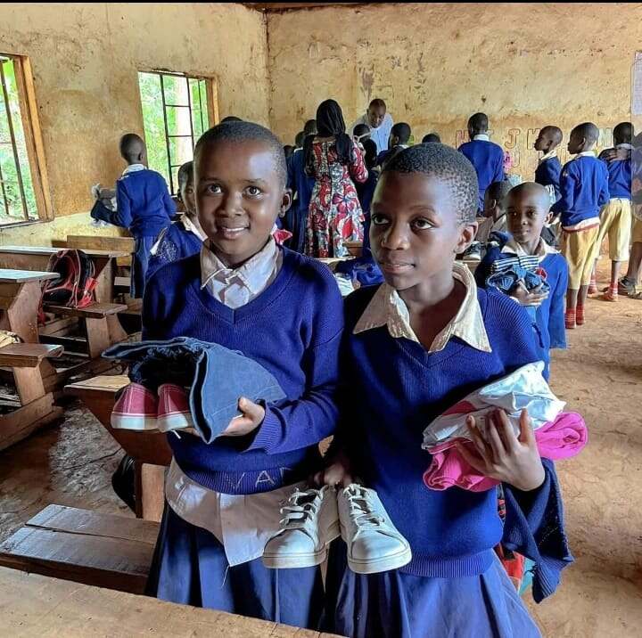 Two pupils in a classroom holding donated shoes and clothing from JOFA