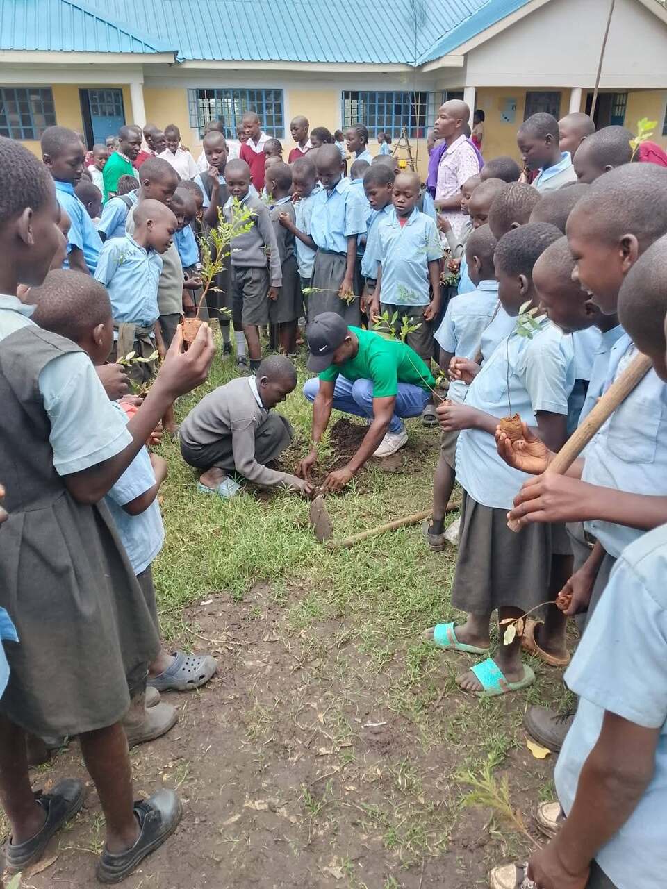 JOFA volunteer in a green Green Action t-shirt planting a tree seedling with a pupil while classmates look on