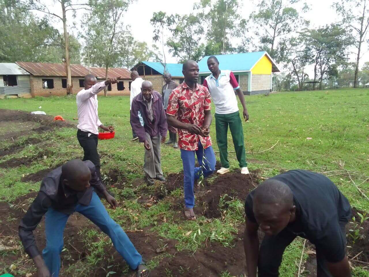 JOFA staff and community volunteers digging planting holes together on a school compound